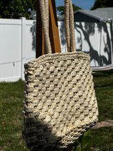 Natural Woven Tote Bag hanging on a wooden post in a sunny outdoor setting.