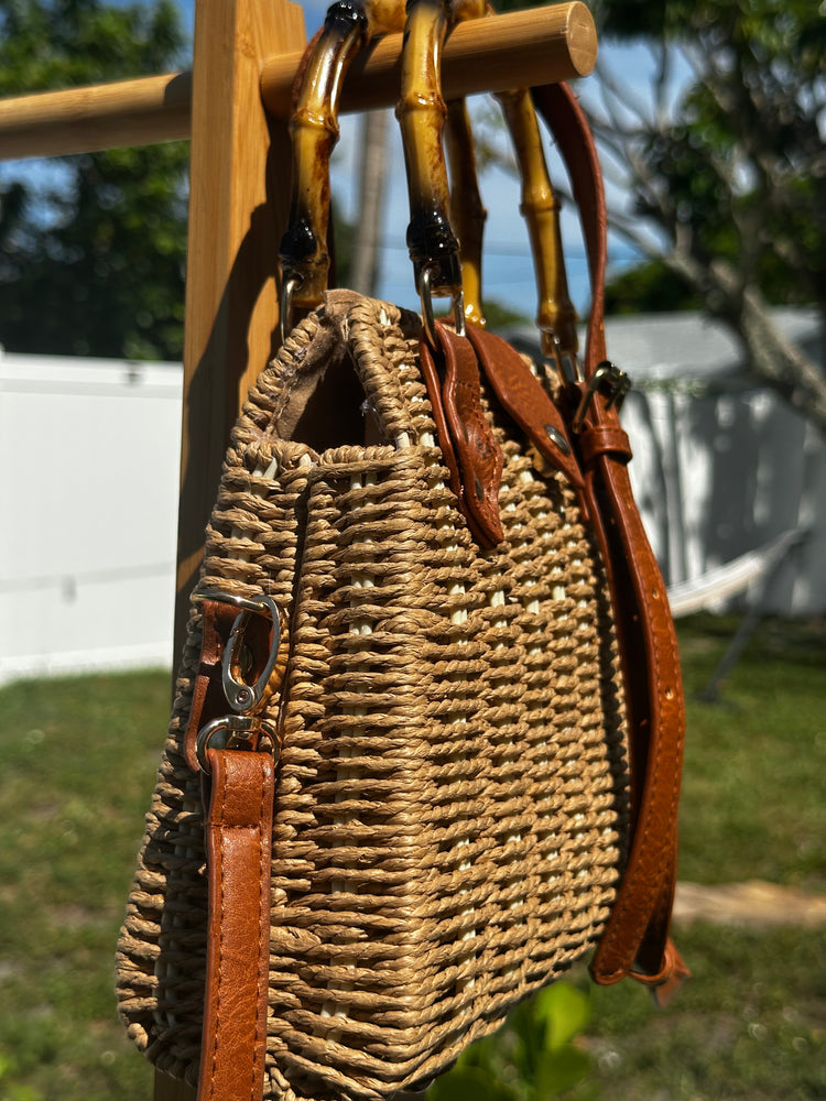 Bamboo Handle Woven Tote with leather straps displayed on a rack outdoors, perfect for stylish beach outings.
