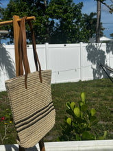 Coastal Stripe Woven Tote hanging outdoors, featuring a stylish design perfect for beach or everyday use.