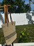 Coastal Stripe Woven Tote hanging outdoors, featuring a stylish design perfect for beach or everyday use.