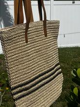 Coastal Stripe Woven Tote hanging outdoors, showcasing its stylish design and durable straps for beach or everyday use.